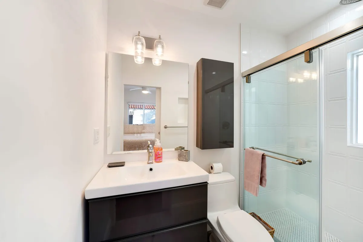 A modern bathroom with a large mirror above the sink, glass-enclosed shower with sliding door, contemporary vanity, and wall-mounted storage cabinet. The space is bright, organized, and exudes a spa-like calm.